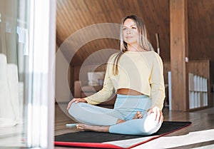 Young slim fitness blonde woman practice morning yoga near window of home