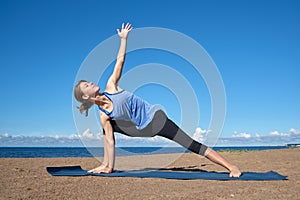 Young slim girl doing yoga on the beach on a sunny morning, stretching before doing sports