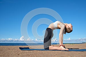 Young slim girl doing yoga on the beach on a sunny morning, stretching before doing sports