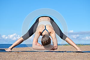 Young slim girl doing yoga on the beach on a sunny morning, stretching before doing sports