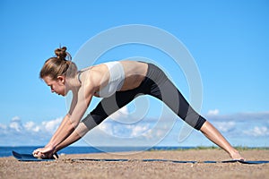 Young slim girl doing yoga on the beach on a sunny morning, stretching before doing sports