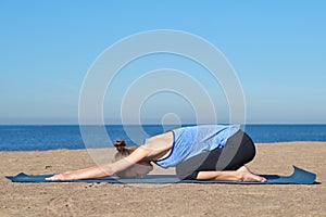 Young slim girl doing yoga on the beach on a sunny morning, stretching before doing sports