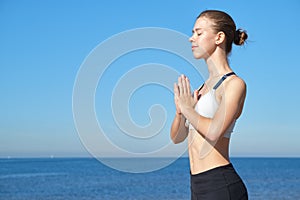 Young slim girl doing yoga on the beach on a sunny morning, sun salutation stand, stretching before doing sports