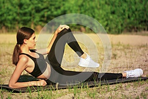 Young slim girl is doing yoga or gymnastics in nature lying on sports mat