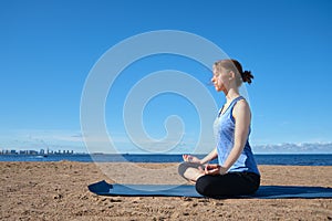 Young slim girl doing yoga, lotus position on the beach, relaxation and meditation