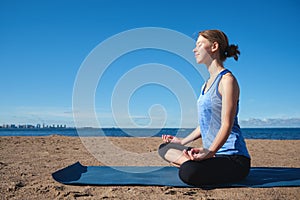 Young slim girl doing yoga, lotus position on the beach, relaxation and meditation