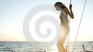 Young slim girl is preparing to jump from a sailing yacht into the open sea on a sunset