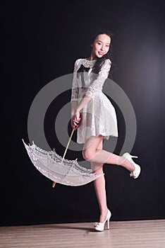 Young slim model in light summer dress with a filigree umbrella posing in studio. Black background