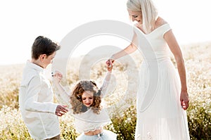Young slim mother plays with her two children in a daisy field