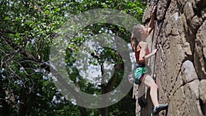 Young slim muscular woman rockclimber climbing on tough sport route, reaching and gripping hold and clipping rope to