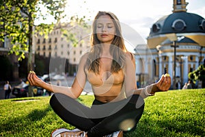 Young slim pretty girl doing yoga on grass in summer park at sunset.