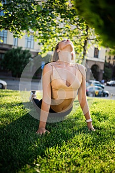 Young slim pretty girl doing yoga on grass in summer park at sunset.