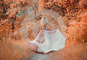 Young slim shapely girl with long blond curly hair wearing a elegant satin flapping silk pink dress with a lace top