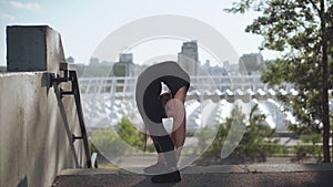 Young slim woman bending backwards in urban city. Wide shot portrait of beautiful slender Caucasian sportswoman training