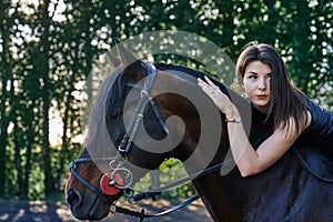 Young slim woman brunette in a black dress sitting on dark brown horse.