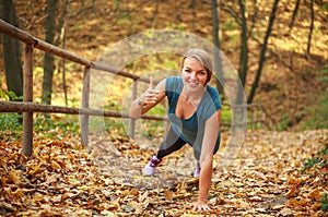 Young slim woman doing fitness exercise stretching in autumn forest park, sport and healthy lifestyle