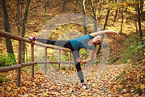 Young slim woman doing fitness exercise stretching in autumn forest park, sport and healthy lifestyle