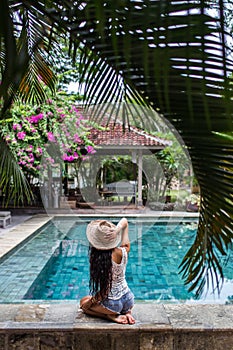 Young slim woman in jeans shorts relaxing near pool with straw hat