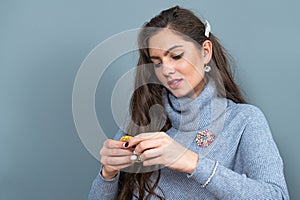 Young slim woman in a long gray sweater looks at jewelry, isolated onngray background, copy space