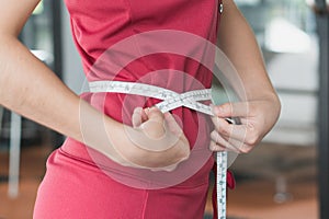 Young slim woman measuring her waist by measure tape