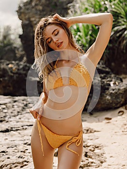 Young slim woman with perfect body in knitted bikini posing at tropical beach.