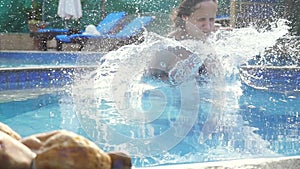 Young slim woman in pink bikini jumping into swimming pool in slow motion and water splashing on beautiful bokeh