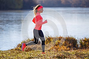 Young slim woman running along the lake in the cold morning