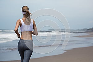 Young slim woman running on the beach. Back view.