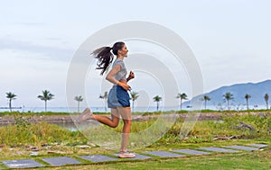 Young slim woman running doing and sport exercises against sunset and beach with palms