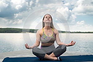 Young slim woman in sportswear practicing yoga near lake, nature