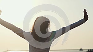 Young slim woman is stretching hands standing against sunrise over sea