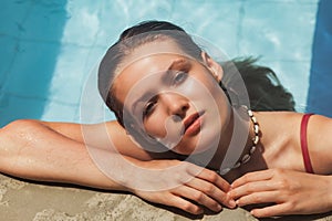 Young slim woman in swimsuit relaxing by swimming pool