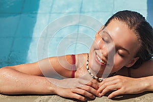 Young slim woman in swimsuit relaxing by swimming pool