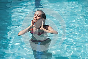 Young slim woman in swimsuit relaxing by swimming pool