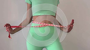 Young slim woman in turquoise spotwear measuring her waist with a tape measure. The concept of diet and weight loss.