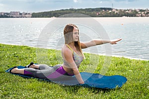 Young slim woman wearing fitness clothes, doing gymnastic exercise on yoga mat near lake