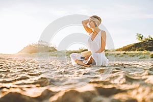 Young slim woman wearing white long dress sit alone at the beach or ocean or sea. Loneliness, divorse. Copyspace.