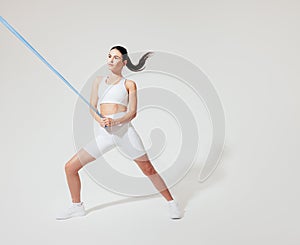 Young slim woman in white fitness wear practicing on a white backdrop
