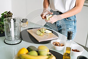 Young slim woman in white t-shirt and blue jeans cooking smoothie with apples healthy food in kitchen at home