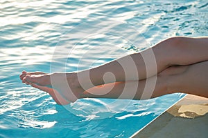 Young slim woman& x27;s legs relaxing near swimming pool in summer sun. Tropical vacation concept