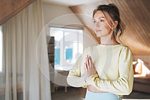 Young sllim fitness blonde woman practice morning yoga near window of home