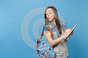 Young sly curious woman student in denim clothes with backpack taking exam peeping, cheating holding notebook pencil