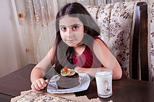 Young small beautiful middle eastern child girl with chocolate cake with pineapple, strawberry, and milk with red dress and dark