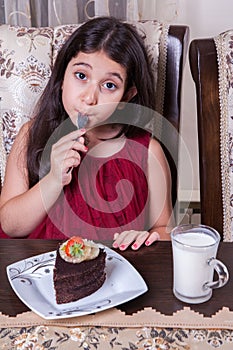 Young small beautiful middle eastern child girl with chocolate cake with pineapple, strawberry, and milk with red dress and dark