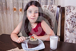 Young small beautiful middle eastern child girl with chocolate cake with pineapple, strawberry, and milk with red dress and dark