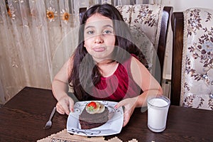 Young small beautiful middle eastern child girl with chocolate cake with pineapple, strawberry, and milk with red dress and dark