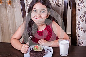 Young small beautiful middle eastern child girl with chocolate cake with pineapple, strawberry, and milk with red dress and dark