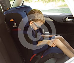 Young small boy sleeping in a child car-seat