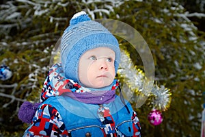 Young small boy walking and having photo shoot in park or forest full of snow in a cold winter day. Male child having