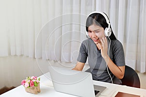 Young smart and active asian female student sitting at table with headset, using computer and taking note for studying online with